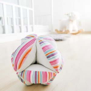 Pelota Montessori de rallas multicolor en combinación con tela blanca sobre piso de madera