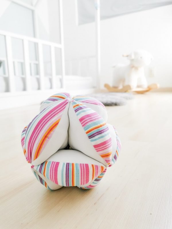 Pelota Montessori de rallas multicolor en combinación con tela blanca sobre piso de madera