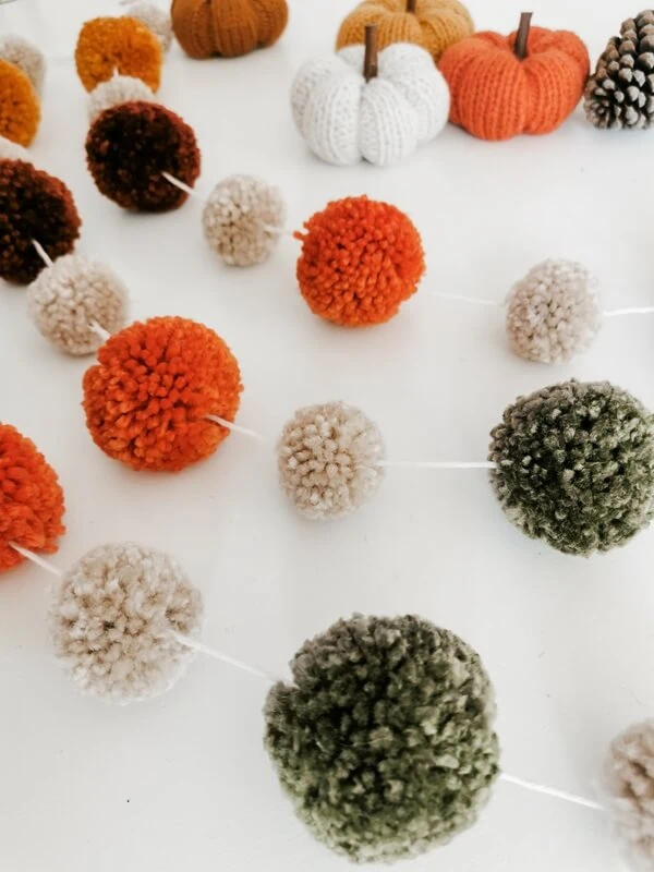 decoracion-de-otoño Detalle de guirnalda de otoño hecha a mano con pompones en tonos verde, beige, naranja y marrón