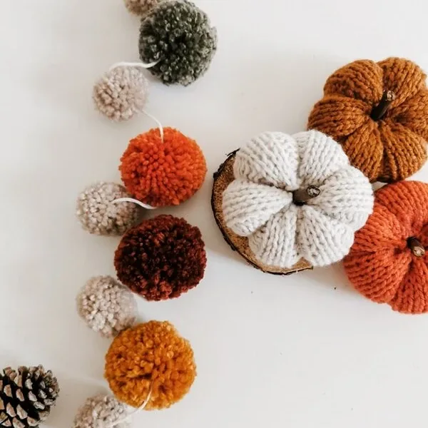 Guirnalda de pompones en tonos otoñales junto a calabazas decorativas tejidas en lana.