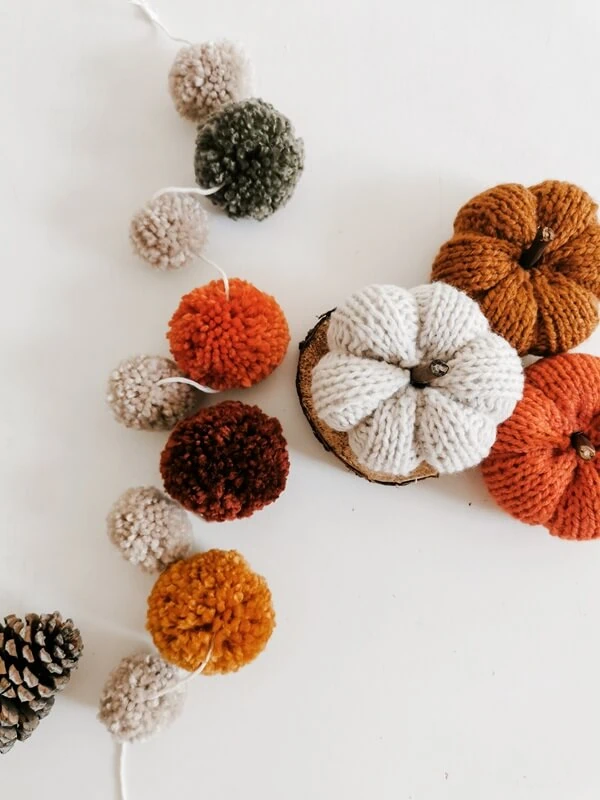 guirnalda-de-otoño Guirnalda de pompones en tonos otoñales junto a calabazas decorativas tejidas en lana.