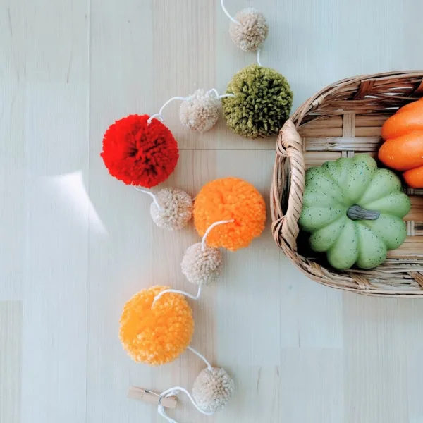 Tira de pompones de otoño junto a una canasta con calabazas
