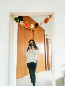 Guirnalda de otoño con pompones en colores tierra y naturales colgada en un espejo de madera clara.