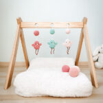Móviles para bebé en crochet con figuras de pájaros en tonos pastel, colgados en un gimnasio Montessori de madera. Son tres colgantes de amigurumi y bolas tejidas.