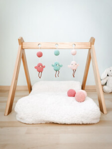 Móviles para bebé en crochet con figuras de pájaros en tonos pastel, colgados en un gimnasio Montessori de madera. Son tres colgantes de amigurumi y bolas tejidas.