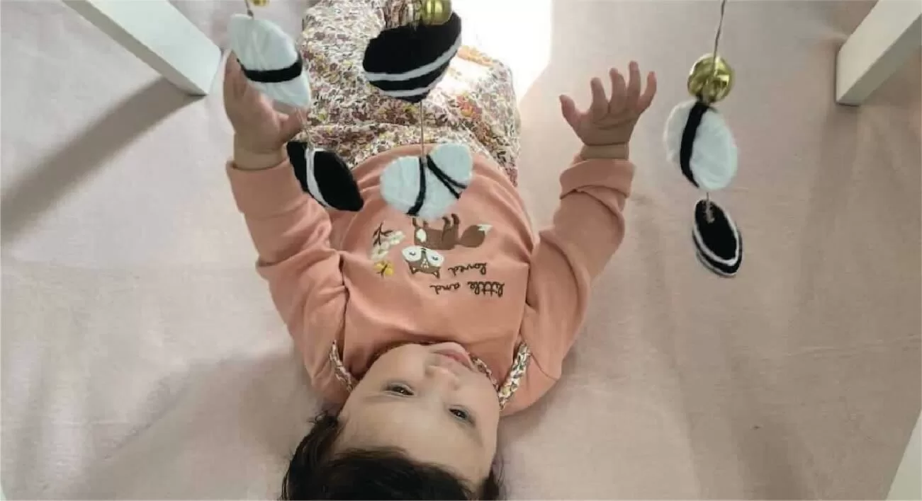 Bebé acostado boca arriba interactuando con un Móvil para bebe en blanco y negro. El móvil cuelga de gimnasio de madera, estimulando la vista y coordinación del bebé.