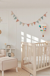 Banderín decorativo de tela en colores vibrantes, colgado en la pared de una habitación infantil. El espacio está decorado con tonos neutros, muebles de madera clara y una guirnalda de banderines pastel, creando un ambiente cálido y acogedor