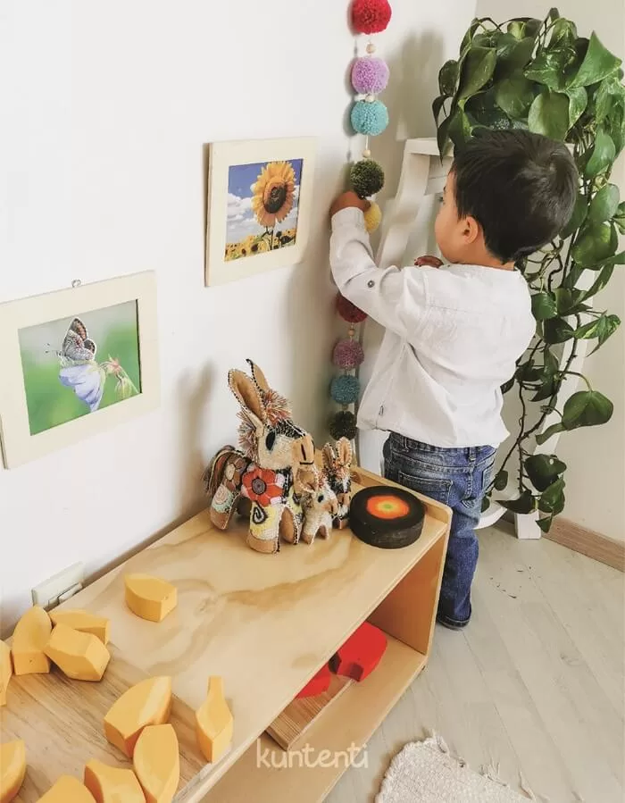 Niño pequeño interactuando de forma autónoma con materiales en un shelf para niños Montessori, fomentando la autonomía infantil en un ambiente preparado