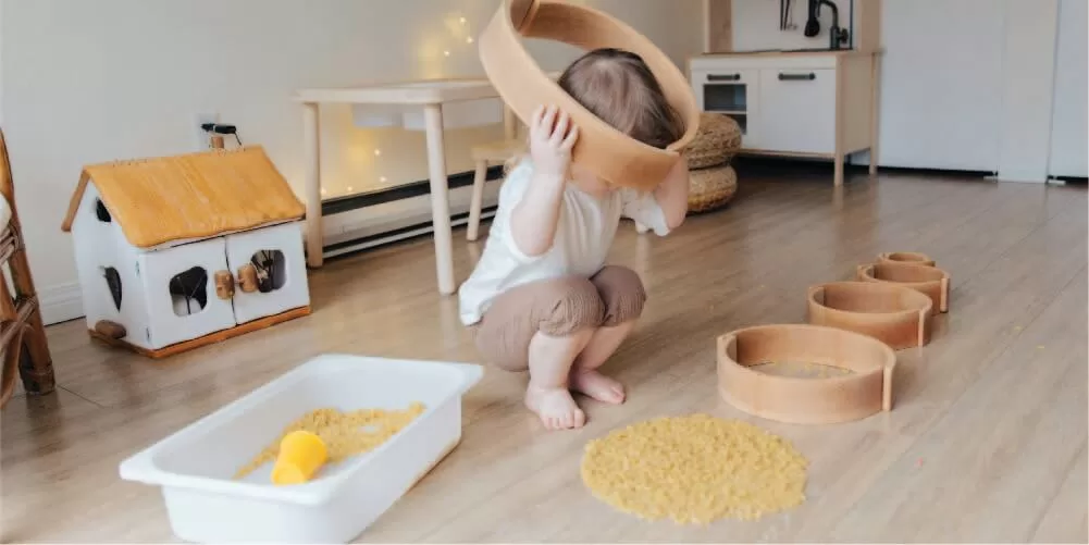 Un niño pequeño sostiene un aro de madera sobre su cabeza, el cuarto en el que se encuentra es de colores neutros, piso y muebles de madera.