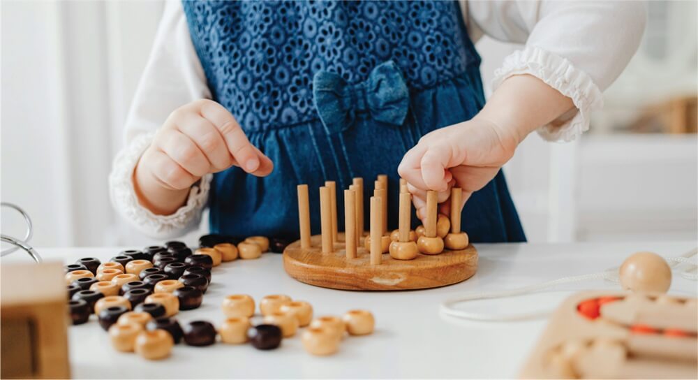 manos de una niña pequeña apilando objetos de madera pequeños, el fondo es de color neutro