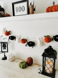 Guirnalda de Halloween con calabazas naranjas, fantasmas blancos y arañas negras acompañada de linterna decorativa y calabazas de colores