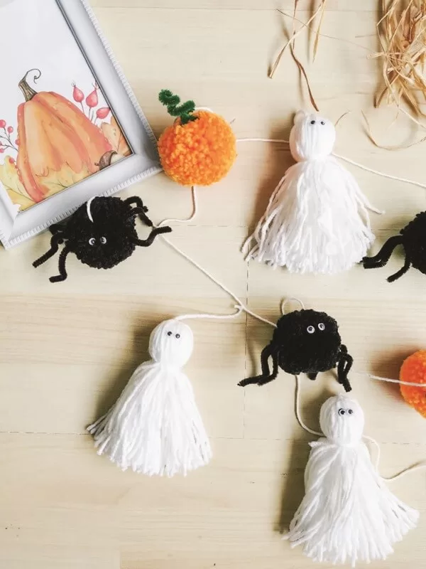 decoracion-otono-hogar-guirnalda-original-halloween Detalle de guirnalda con pompones de hilo en forma de calabazas y fantasmas, ideal como decoración de Halloween con estilo minimalista y natural.
