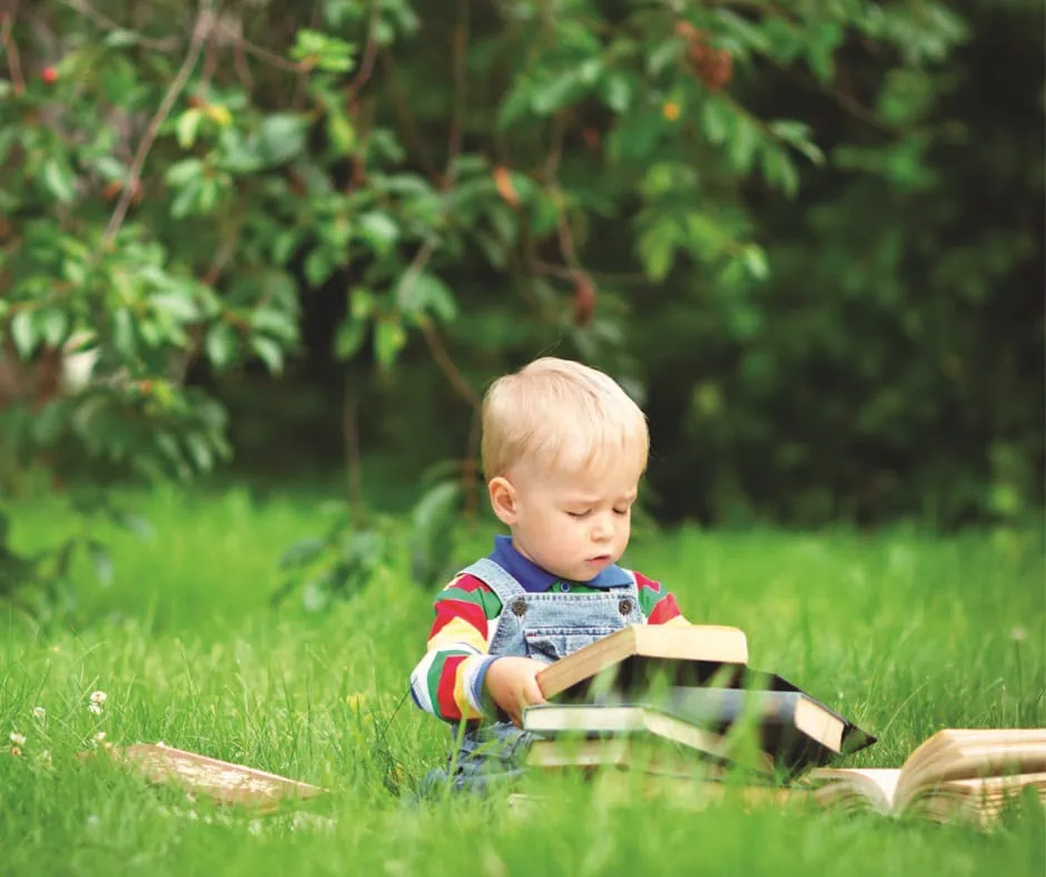 Niño pequeño leyendo un libro en el jardin de la casa, fomentando la lectura en casa.