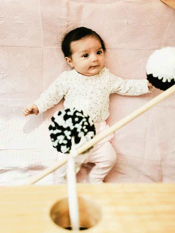 Bebé sobre superficie suave en color palo de rosa mirando un movil blanco y negro