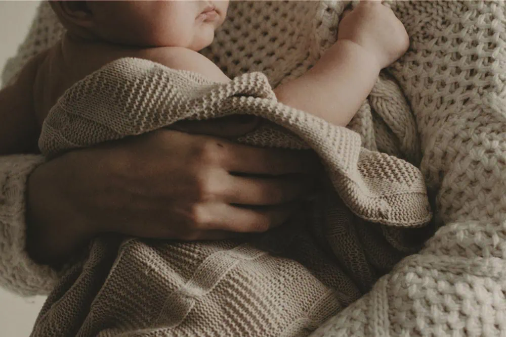 bebe envuelto en manta tejida siendo abrazado